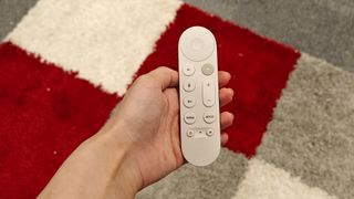 Google TV Streamer video streamer remote control held in hand above red, grey and white rug