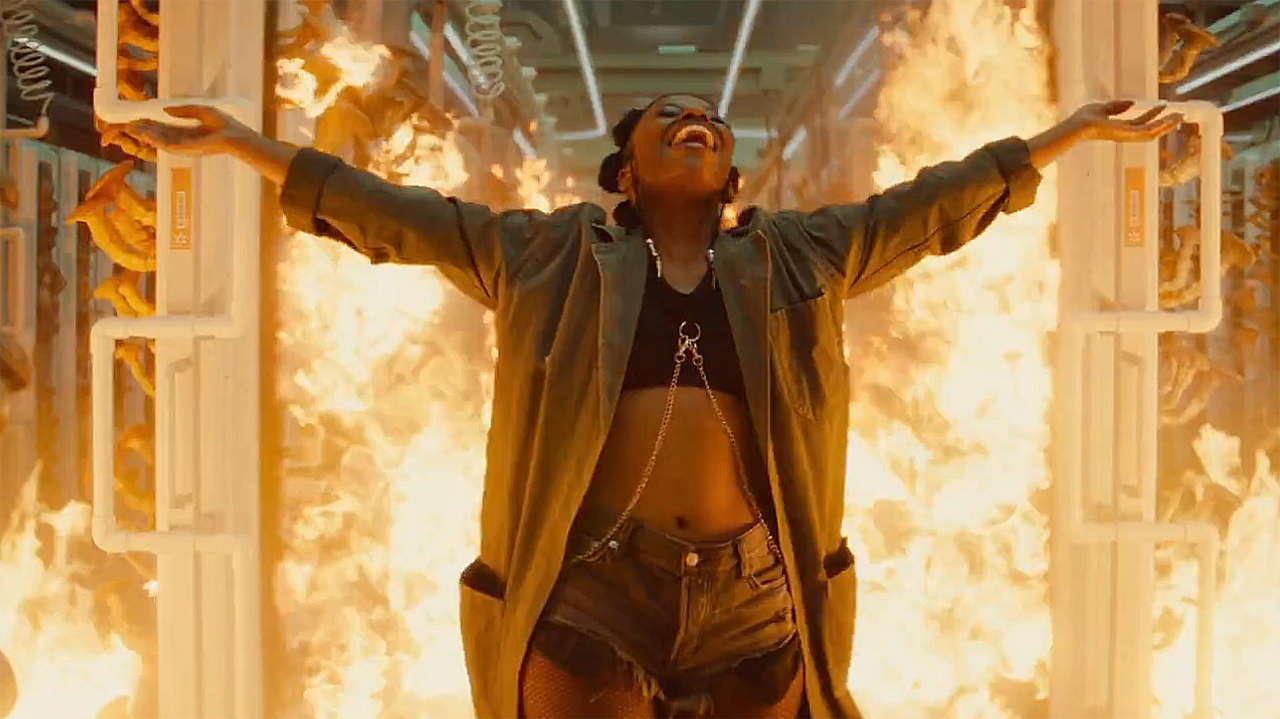 Clown smiling with her arms held out in front of a fire in Marvel's Ironheart TV show
