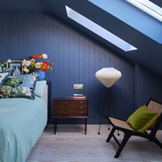 small bedroom colour ideas, navy loft bedroom with blue walls and ceiling, small vintage side table, floor lamp, chair, pale blue bedding, patterned cushions, vase with poppies 