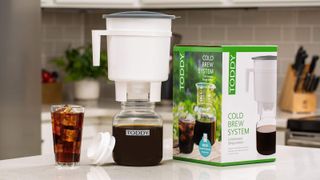 A cold toddy coffee maker by its box and a glass of coffee on a kitchen countertop
