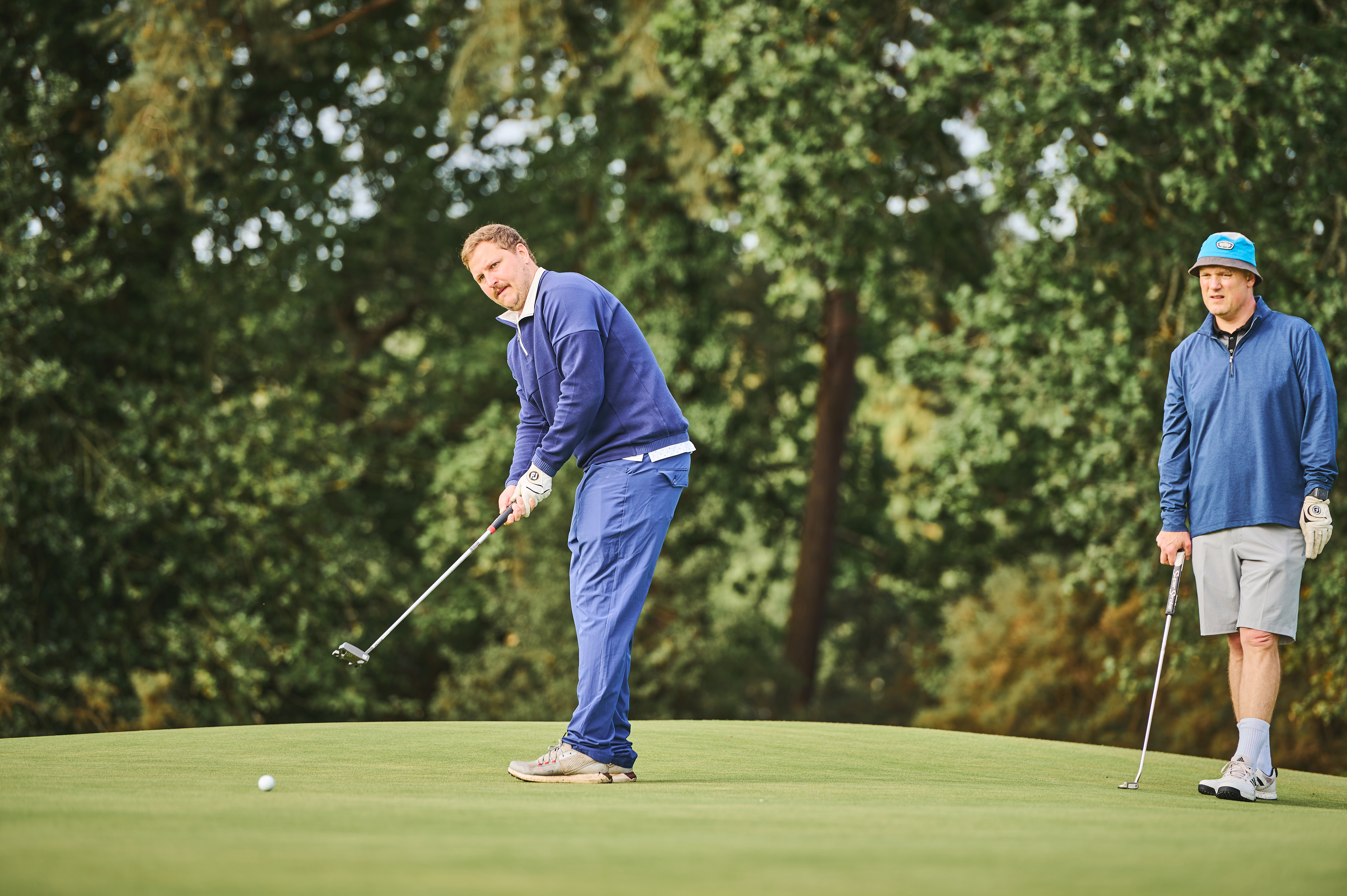 A golfer putting on a green and being watched by a playing partner