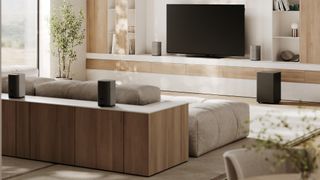 Loewe We.BOOST home cinema audio system showing four speakers and a subwoofer in a brightly lit living room