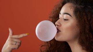 A woman pointing at blowing a bubble with chewing gum