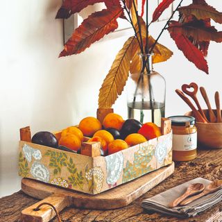 An autumn table setting with seasonal foliage in a vase and a crate of fruit