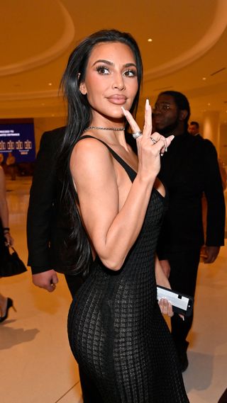 Kim Kardashian holding up a peace sign in a black knit gown
