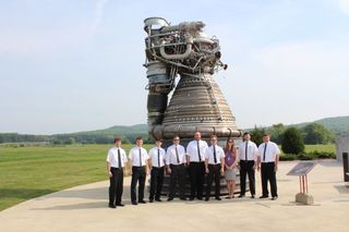 Engineers dressed in Apollo-style white shirts and thin black ties stand by an F-1 engine at NASA’s Marshall Space Flight Center in Huntsville, Ala.