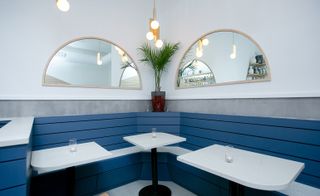 Booth featuring the blue wooden panelling, white tables and framed, semi-circular mirrors