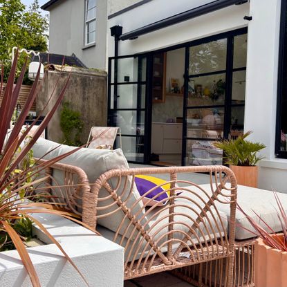 patio with open doors, planting, a crank awning and a grey outdoor sofa