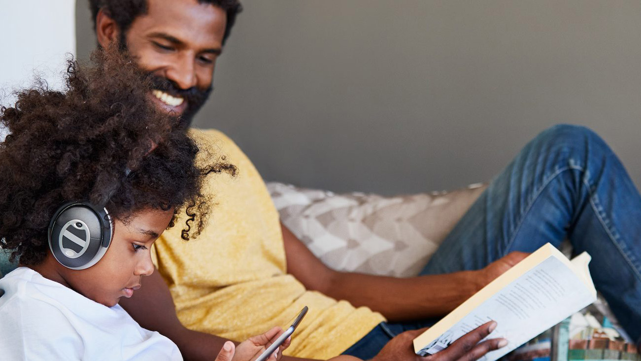 a parent reading while a child listens to spotify on headphones