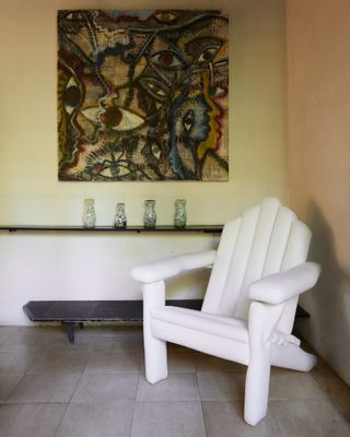 Forefront is a white chair with a prism shape back. A painting on the wall with various eyes.