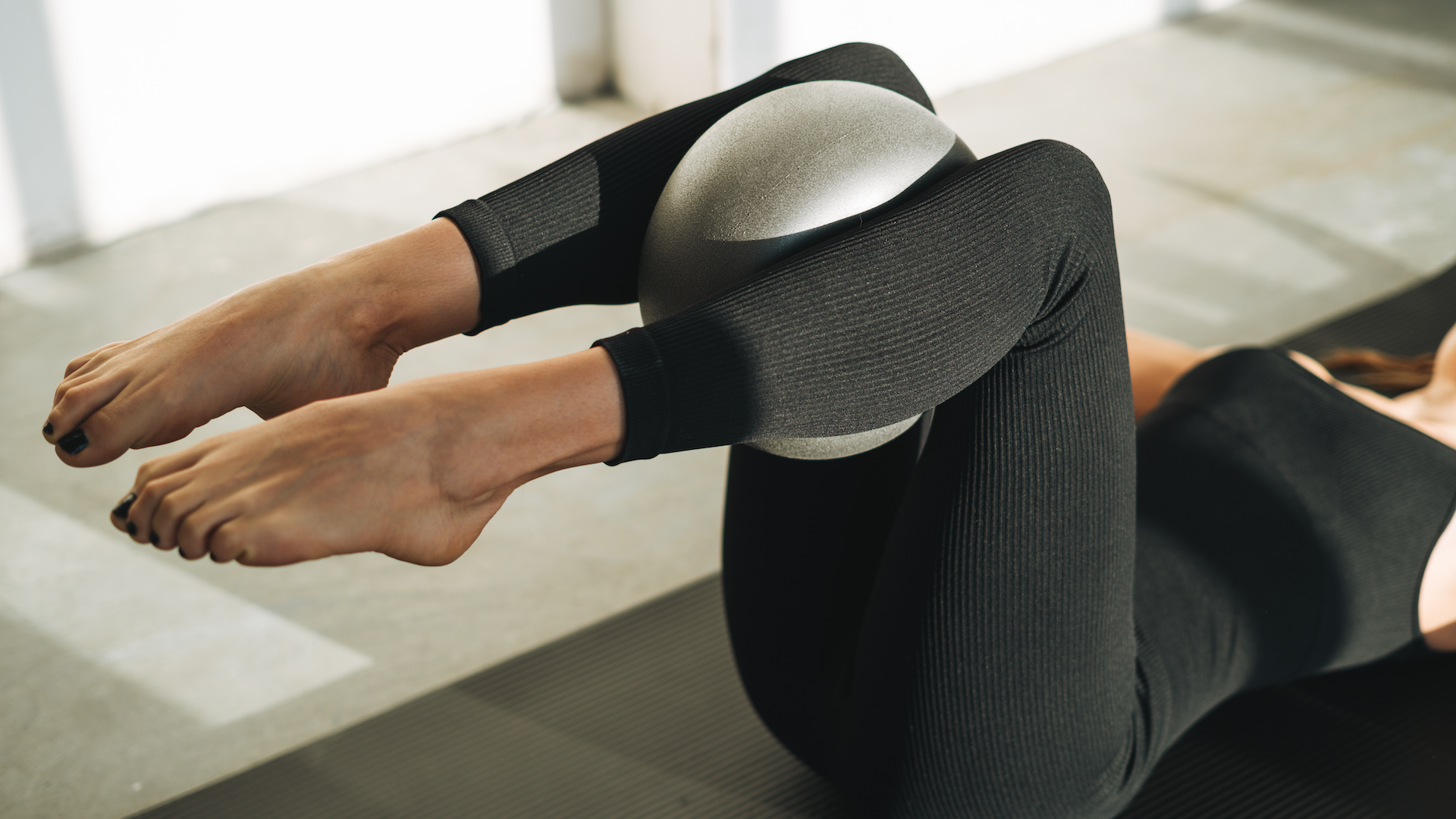 Woman doing mat Pilates with a ball