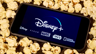 The Disney Plus logos on a phone surrounded by popcorn