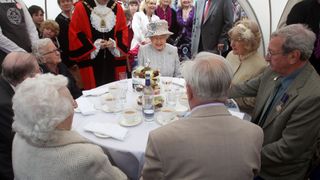 Queen Elizabeth II sits down at a table of couples enjoying their 60th Wedding Anniversaries