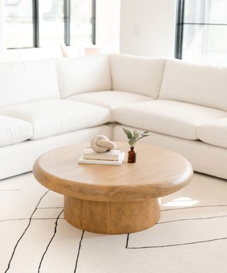 A round wooden table next to a white couch with a white rug underneath it