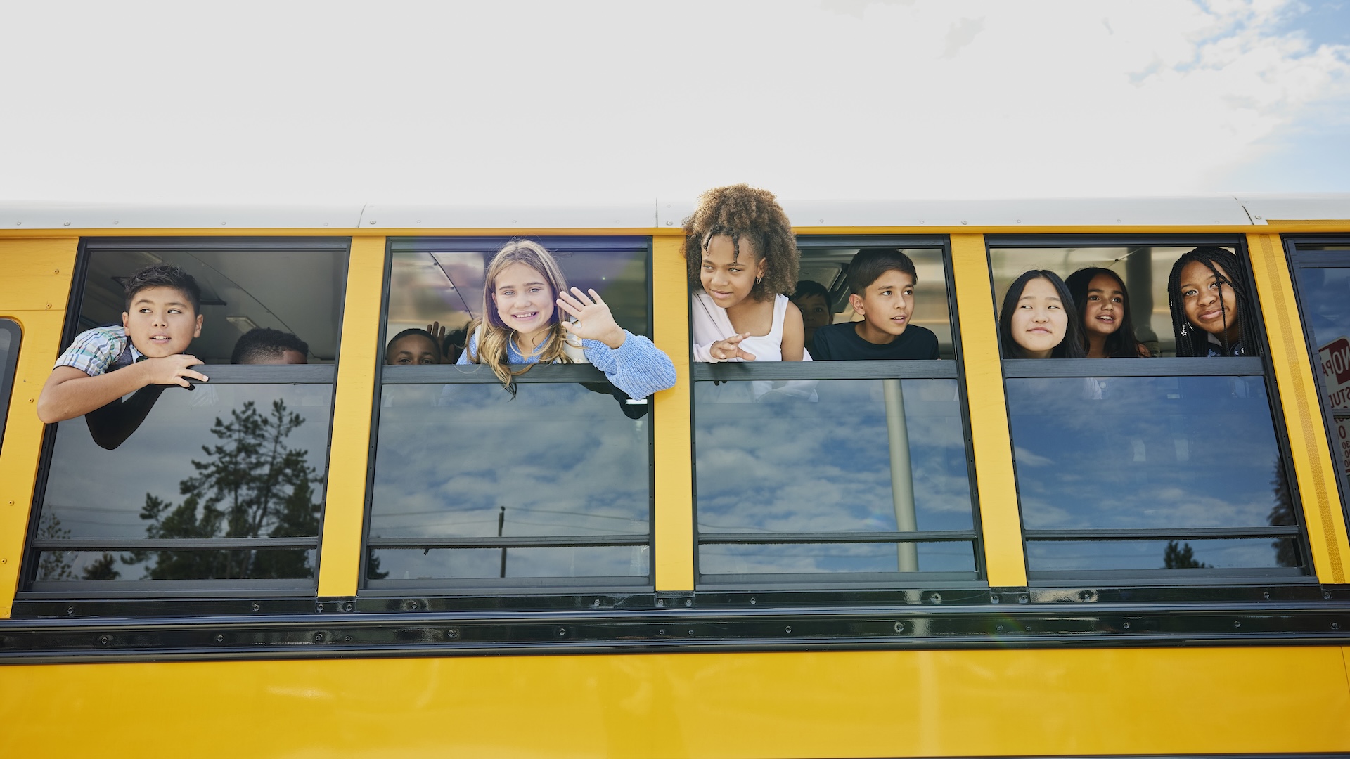 a group of smiling children hang out the school bus windows