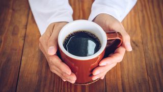 Image shows hands holding mug of black coffee