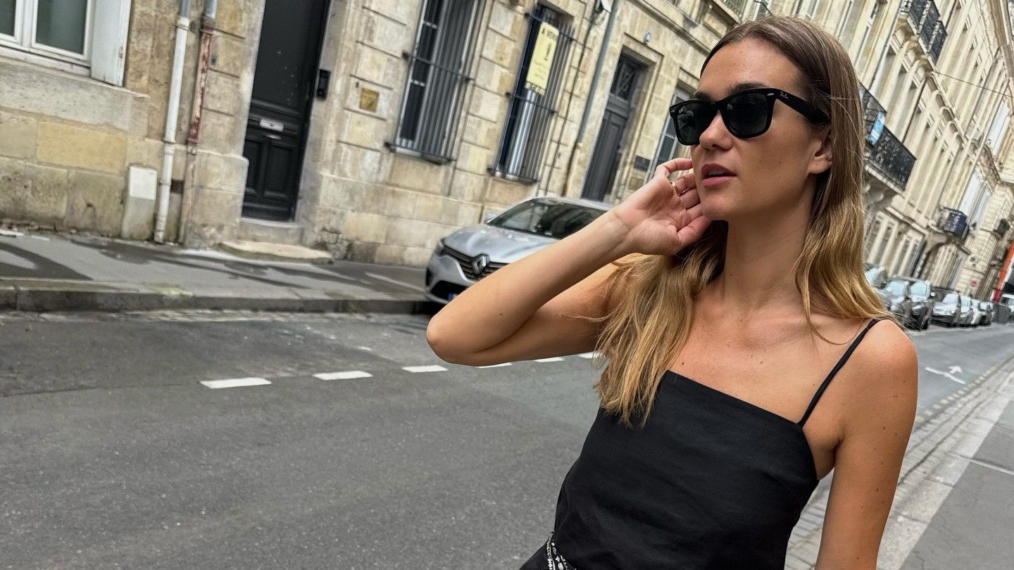 Woman wears a little black dress with a silk scarf tied at the waist. 