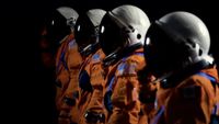 four spacesuits stand with white helmets.