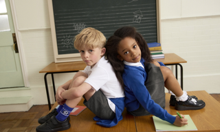 Two school children back to back in a class room wearing Marks & Spencer school uniform