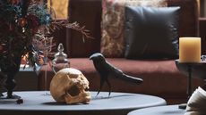 Close up of Halloween decorations including a skull and crow on a black coffee tablein a dark moody living room with candles and dark florals