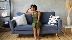 A woman sitting on her sofa looks regretful as she looks off to the side.