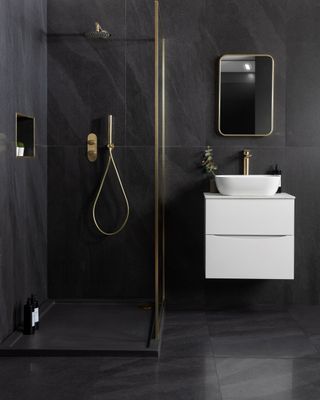 An all black bathroom with large format glossy black wall and floor tiles, a glass shower enclosure and a white floating sink unit