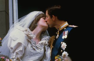 Princess Diana wearing a white wedding dress and veil kissing Prince Charles on their wedding day