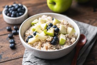 A bowl of porridge topped with green apple, hemp seeds and blueberries.