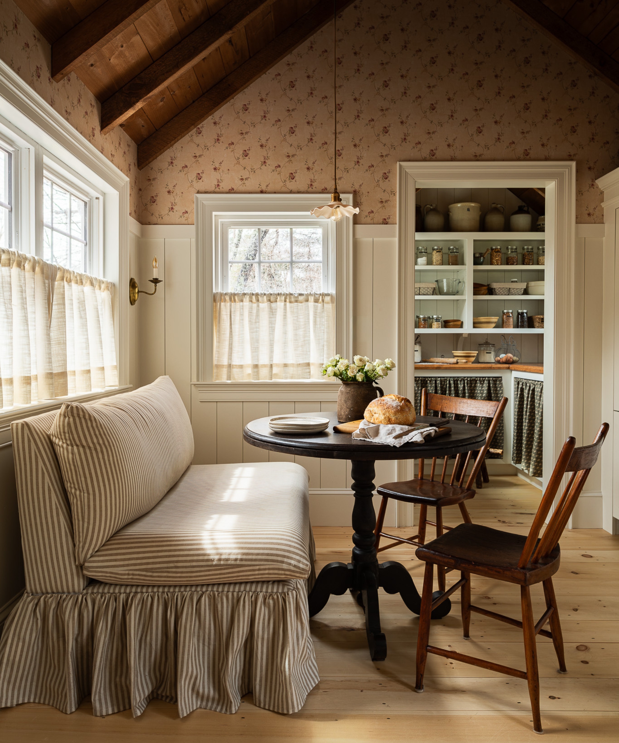 A small kitchen featuring a dinette with a stripe armless sofa seating with a skirted base, and small round pedestal table, and two wooden chairs
