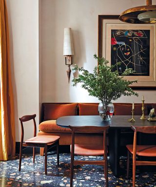 Dining room with terrazzo flooring, wood and leather dining chairs, banquet seating with orange cushions, oval black dining table, artwork and greenery