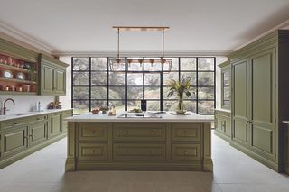 A bright green kitchen with an island in the middle of the room and crittall windows looking into the garden