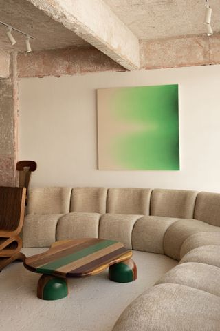 Large curved sofa in an all beige living room with a bright green abstract painting hanging on the back wall over the sofa