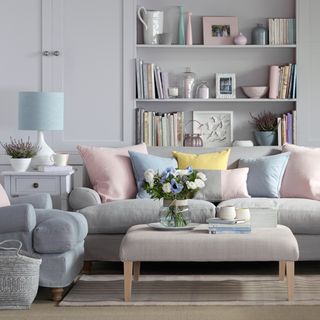 pale grey wall with shelving and sofa with cushions and flower vase