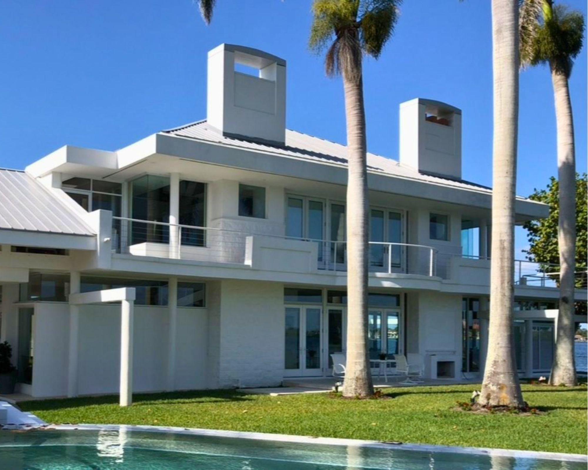 Mark Famiglia's white Sarasota property with blue skies, and a green lawn, palm trees, and a pool in the foreground.