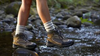 Woman crossing stream wearing hiking boots