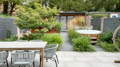 back garden with a dining area, hot tub and studio among green plants