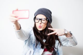 Pretty hipster girl taking selfie and making duck face. Sending kisses and holding peace sign.