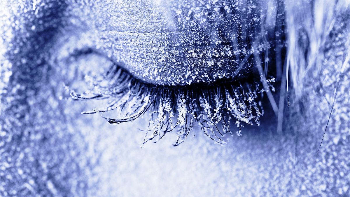 A close-up of a woman&#039;s closed eye with blue frost covering her face and eyelashes