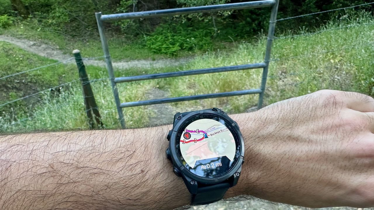 A Garmin Fenix 8 showing a course map saying to make a turn in front of a metal fence surrounded by barbed wire.
