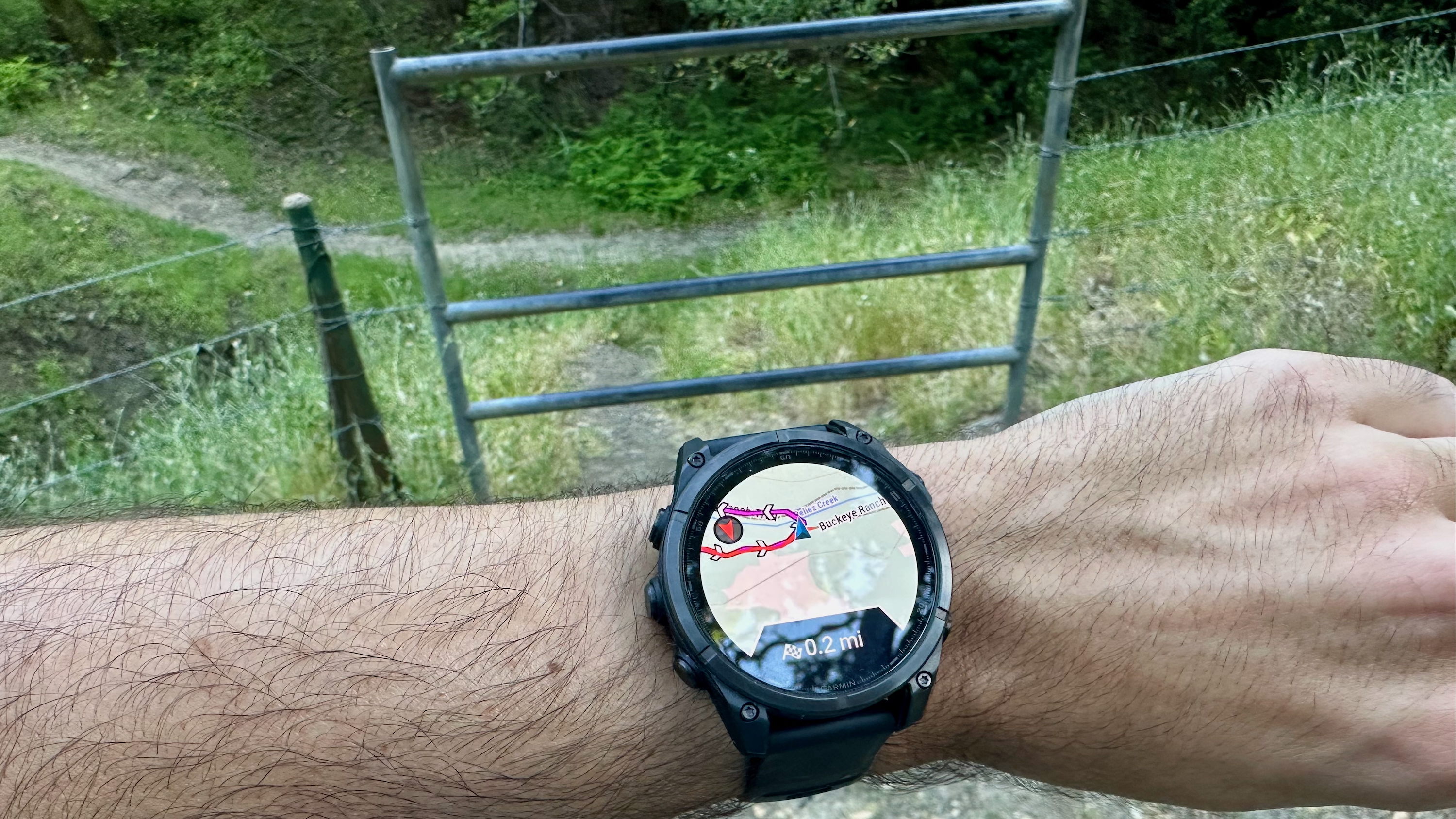 A Garmin Fenix 8 showing a course map saying to make a turn in front of a metal fence surrounded by barbed wire.