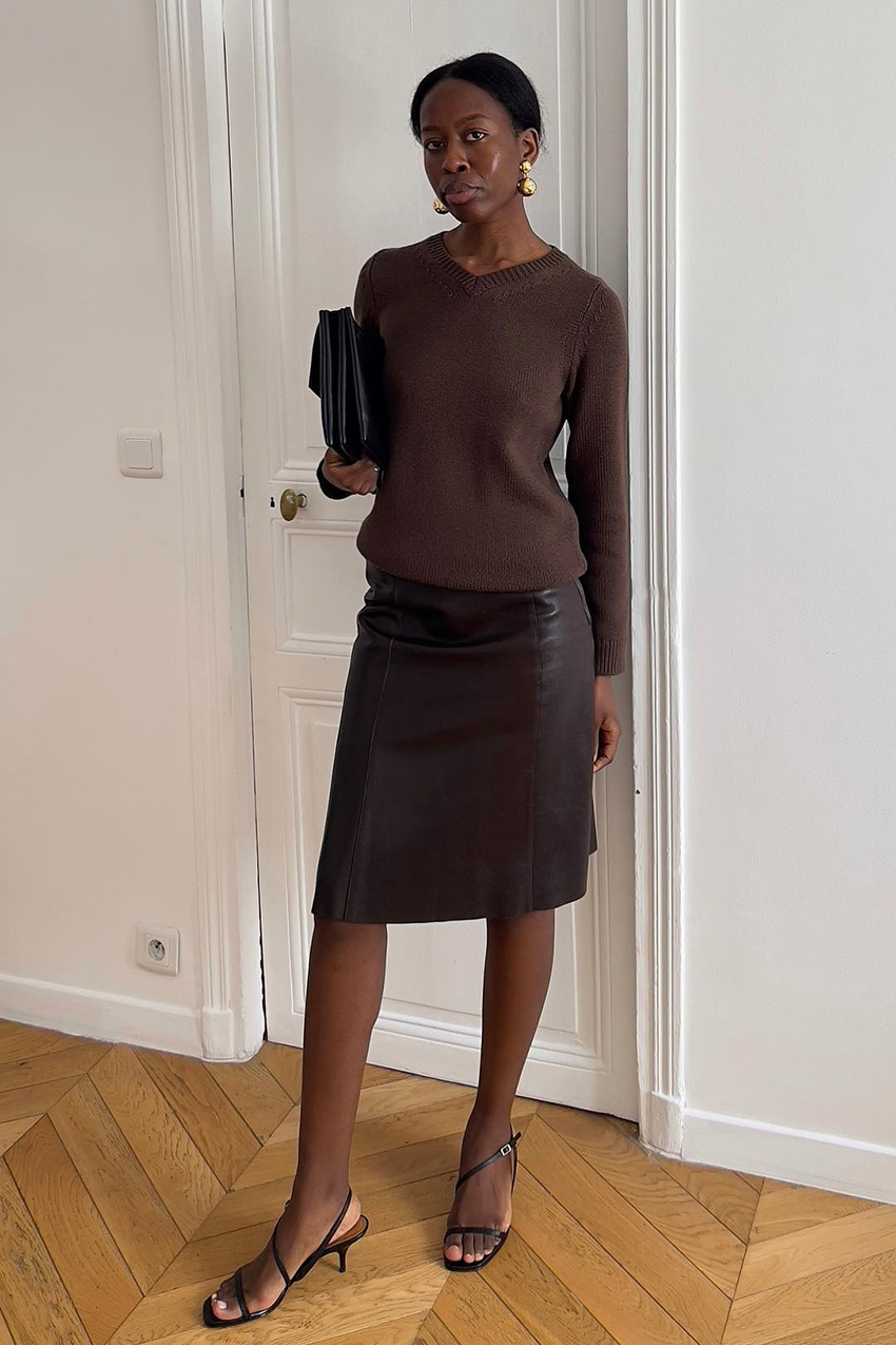 a woman wearing brown v neck sweater, brown leather skirt, and black strappy sandals