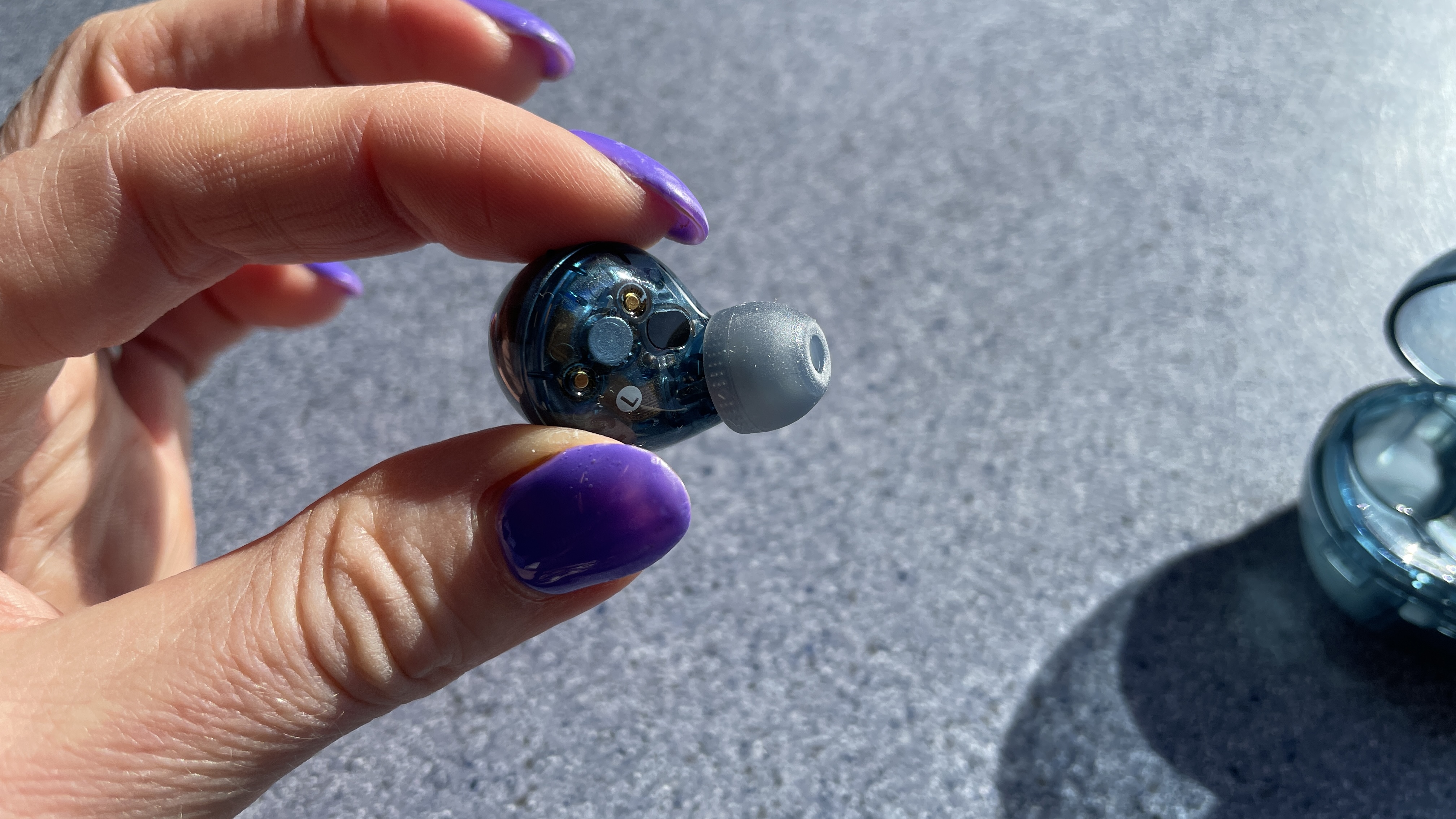 Sony WF-C710N earbuds in 'blue glass' on a grey table, with a woman's hand holding one of the earpieces
