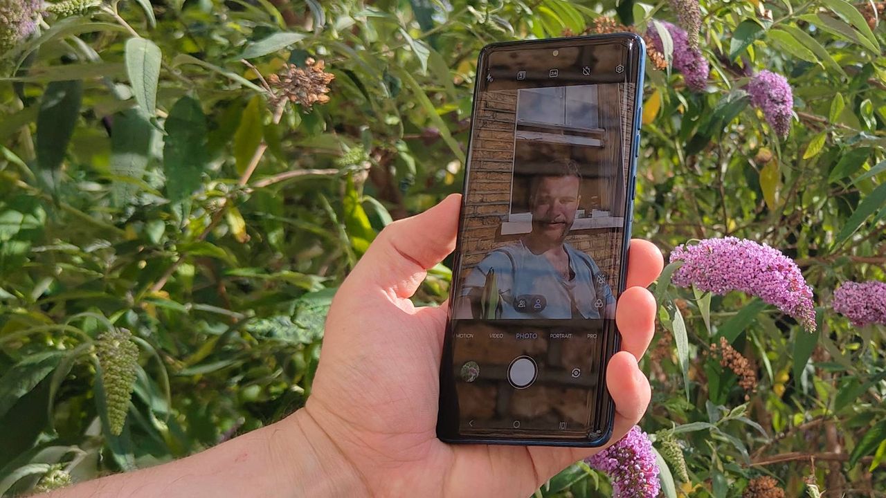 The Motorola Edge 60 in front of a flowery bush.