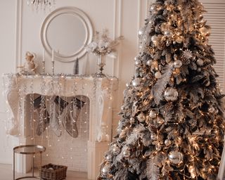 a white and silver elegant christmas display in a small living room with a white fireplace