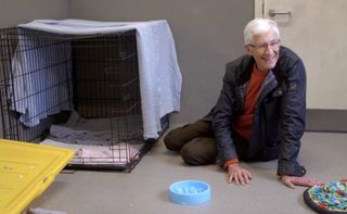 Paul O'Grady sitting next to an empty dog cage