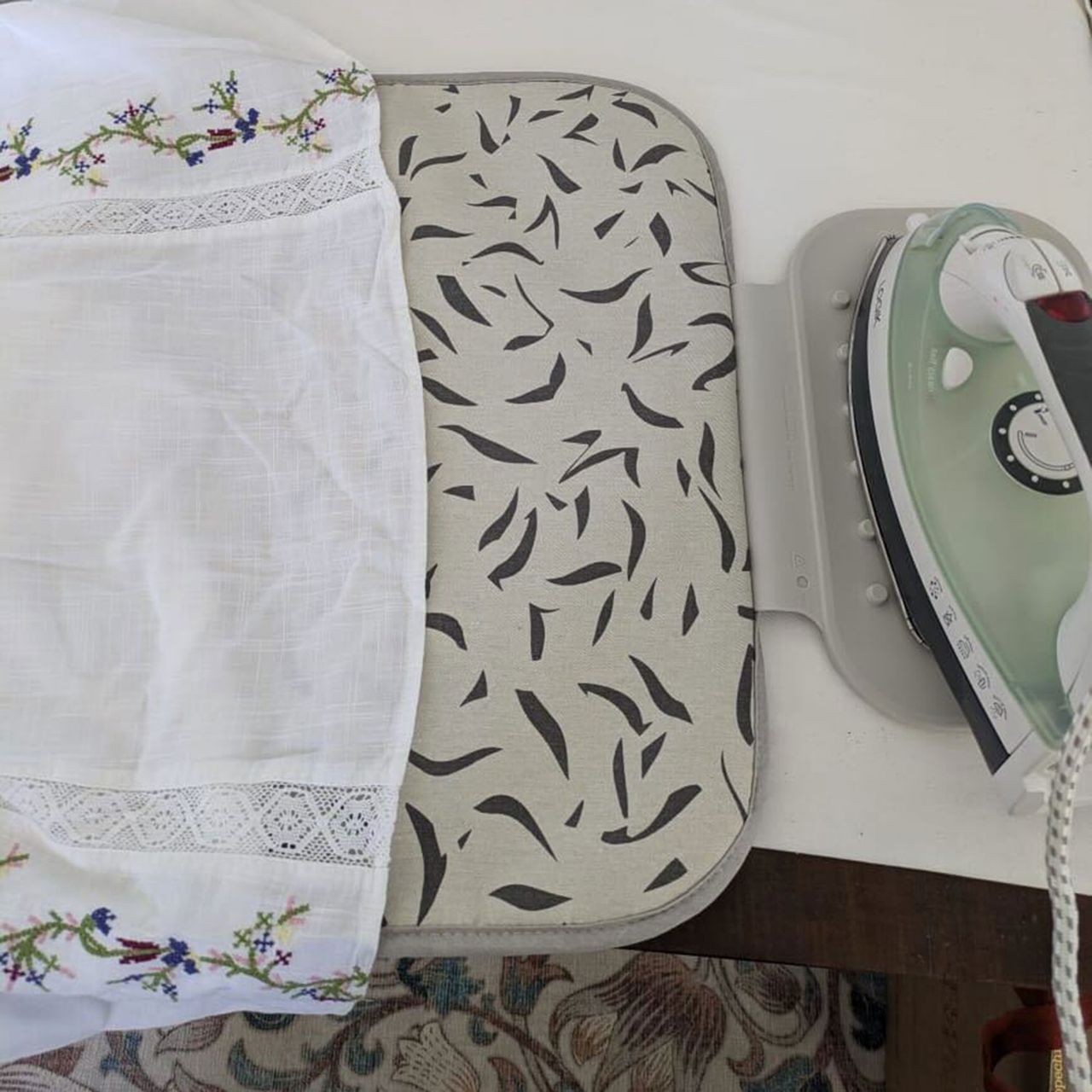 Grey patterned ironing mat on table with iron resting on silicone section
