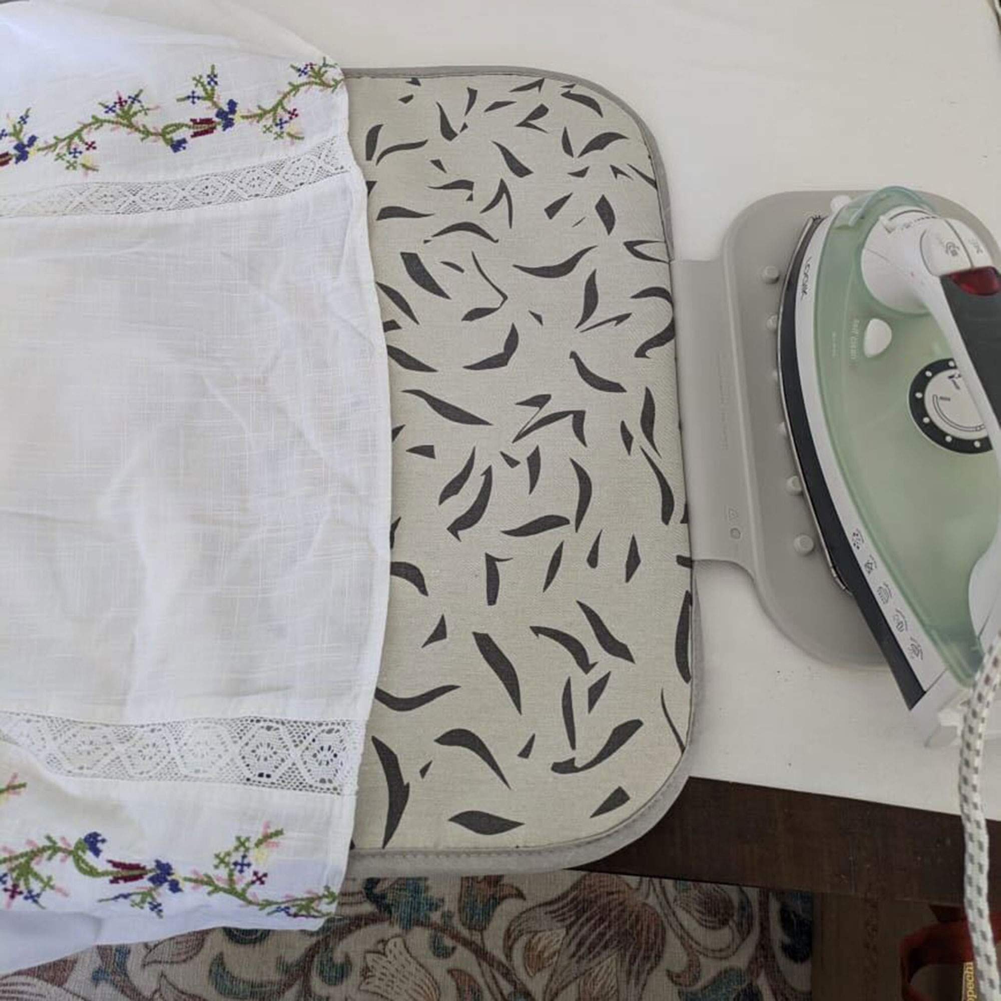 Grey patterned ironing mat on table with iron resting on silicone section