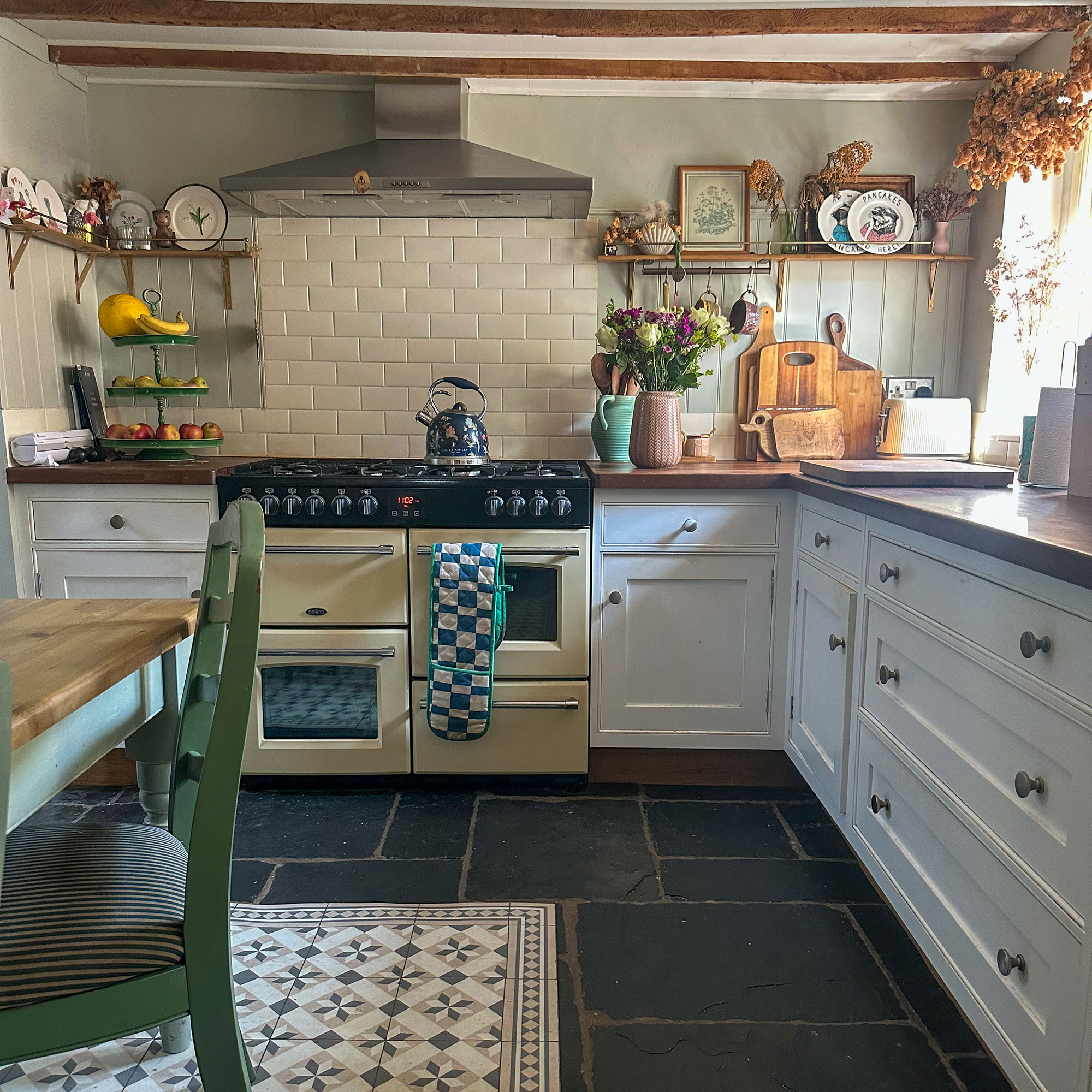 Country kitchen with pale blue cabinetry, flagstone flooring, range cooker and wooden ceiling beams