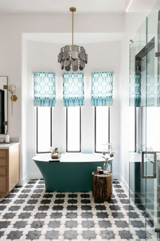 Bathroom with black and white tiled floor, green freestanding bath and blue patterned blinds