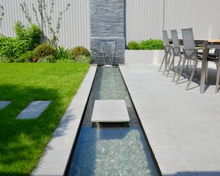 stepping stone over stream with wall water feature in garden designed by Tom Howard